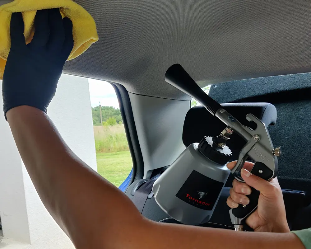 Osoba używająca pistoletu natryskowego do czyszczenia wnętrza samochodu.